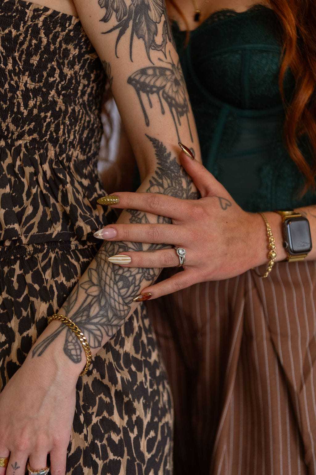 Tattoos on arms in elegant outfits, showing gold accessories and a smart watch.