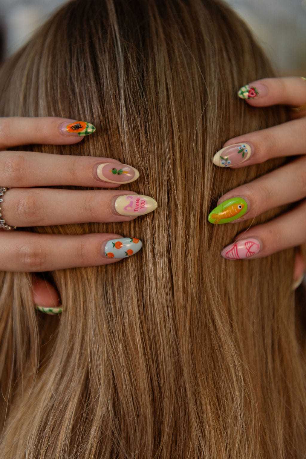 Colorful nail art with floral and abstract designs on hands against long, straight hair.